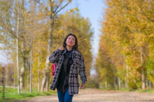 outdoors lifestyle portrait of young happy and pretty Asian Japanese woman walking relaxed and cheerful at beautiful city park in vibrant yellow and orange Autumn tree leaves