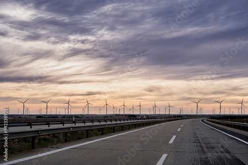 lonely highway at sunrise with a line of windmills on the horizon and soft orange and blue clouds