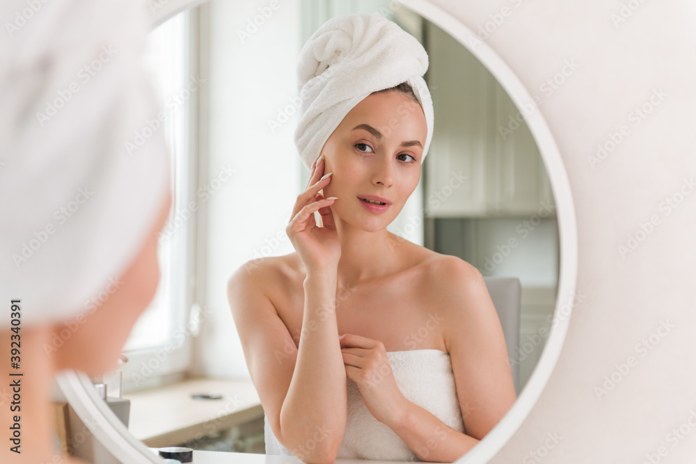 Young female reflected in mirror standing in bathroom and applying cosmetic patches under eyes during daily morning beauty procedure. Young woman applying collagen patches under eyes. Young female reflected in mirror standing in bathroom and applying cosmetic patches under eyes during daily morning beauty procedure. Young woman applying collagen patches under eyes.