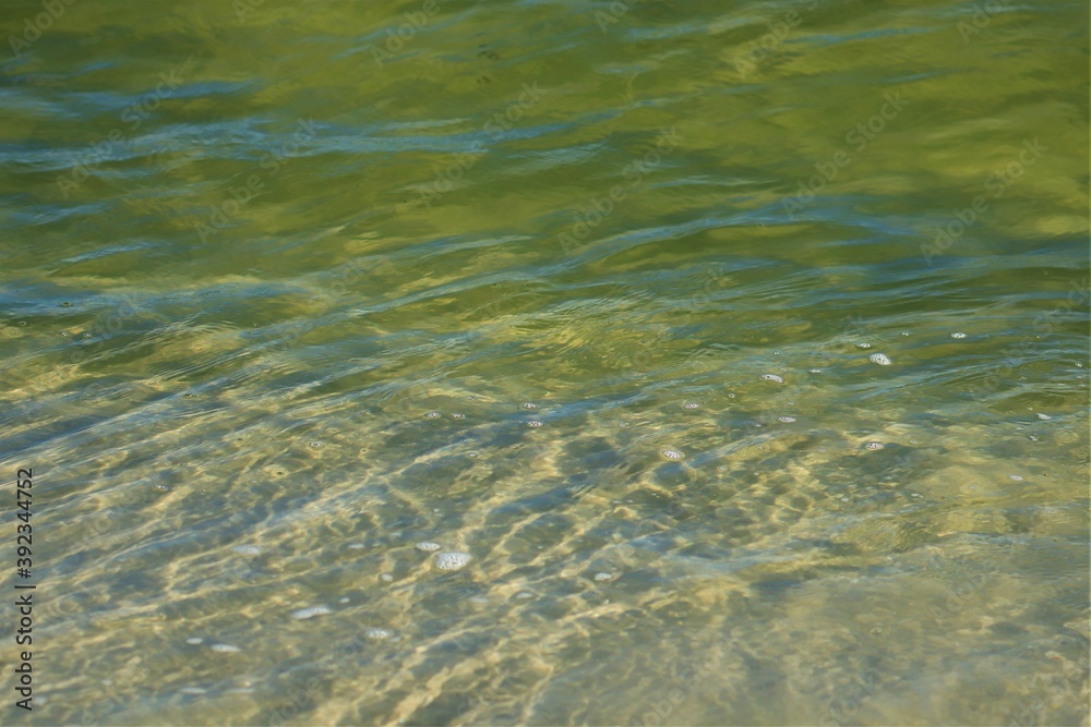 Ripples on the water, sea water near the coast, sand is visible through the water, top view