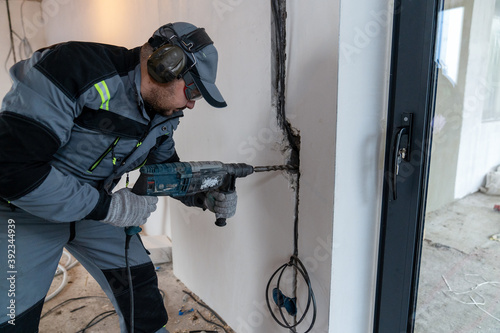 a worker drills a hole in the wall with a puncher for wires
