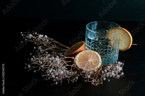 Alcohol drink  gin and tonic cocktail  garnished with lemon fruit and flower isolated on black background. Iced cocktail drink with lemon and herbs.
