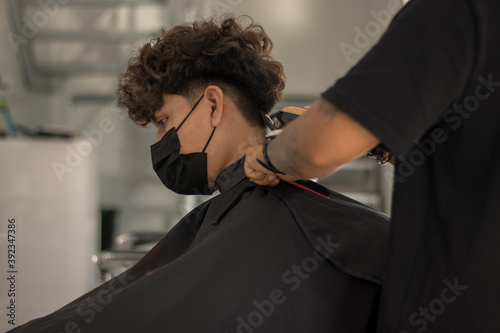 Session in a hair salon with a young hairdresser with a mask cutting the hair of a boy with a mask in times of pandemic photo