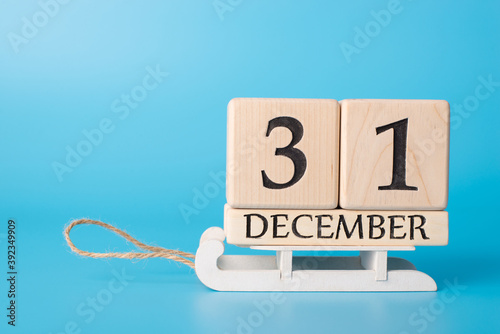 Close up photo of wooden cube calendar showing the last day of old year standing on little white wooden sledge isolated on blue background