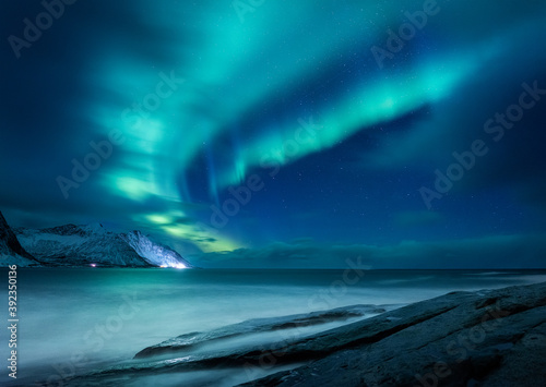 Fototapeta Naklejka Na Ścianę i Meble -  Aurora borealis in Norway. Green northern lights above mountains and ocean. Night winter landscape with aurora. Natural p henomenon background in Norway.
