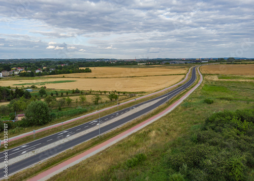 Aerial view of Long highway between yellow wheat fields at cloudy day