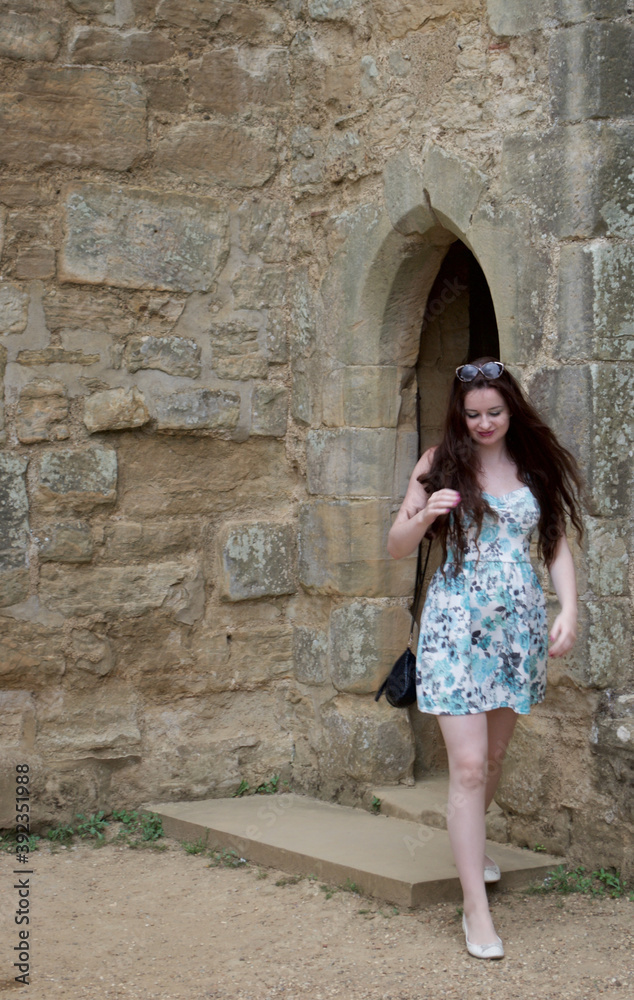 Long haired brunette teenage girl walking through ancient stone archway