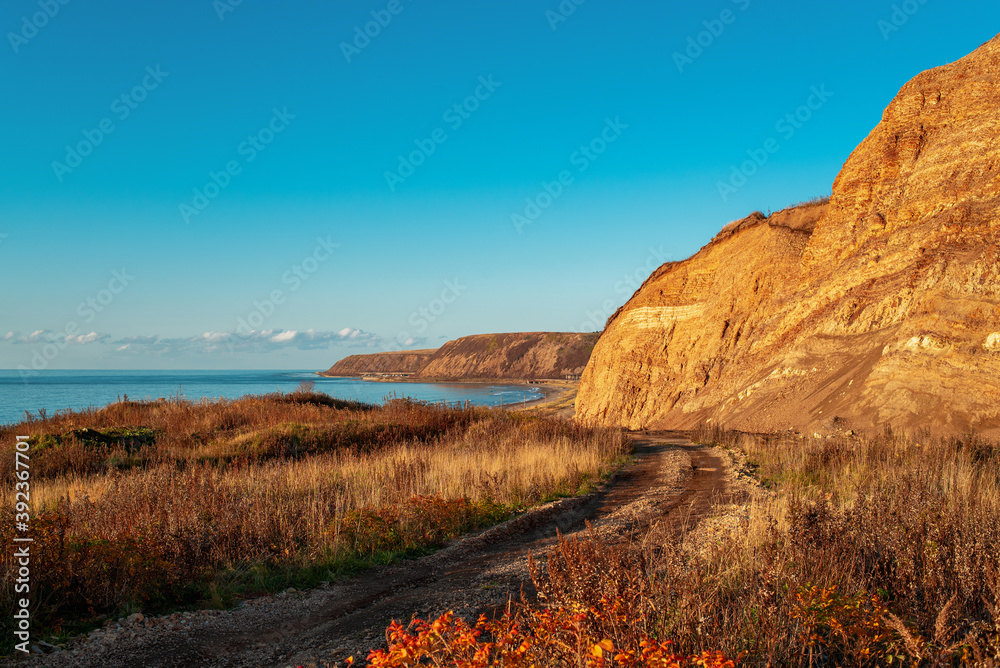 Beautiful colorful layered rock formations on sunset. Road to the sea coast. Sea on the horizon. Scenic landscape with clear blue sky. Natural background with copy space. Russia, Sakhalin Island.