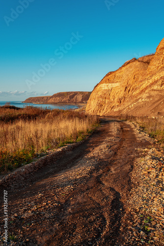 Beautiful colorful layered rock formations on sunset. Road to the sea coast. Sea on the horizon. Scenic landscape with blue sky. Natural background. Vertical view. Russia, Sakhalin Island. Copy space.