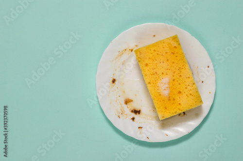 Dirty white plate and sponge with cleaning gel on a blue background.