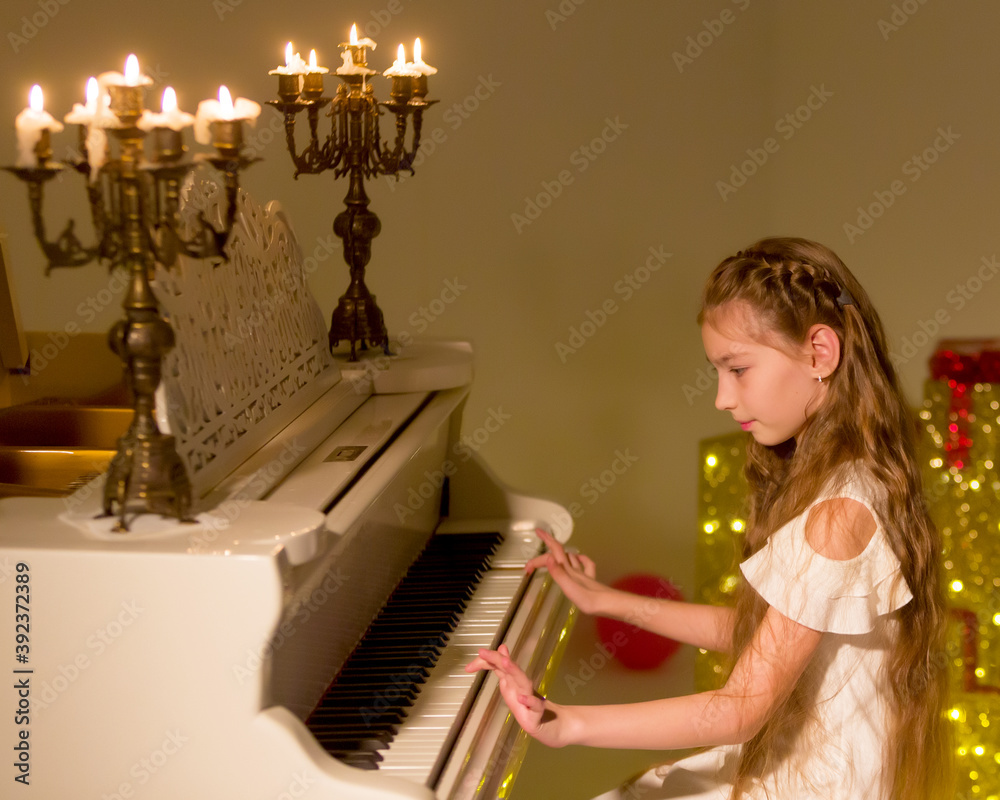 Obraz premium Little girl plays the piano by candlelight.
