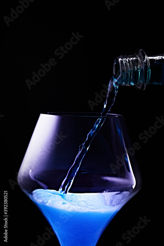 Blue drink is poured into a glass. Black background.