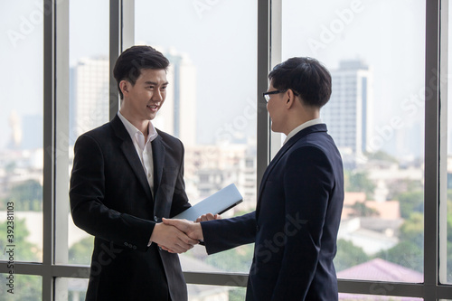 Negotiating business,Image of businesswomen Handshaking. young asuan businessmen shaking hands together while standing by windows in an office