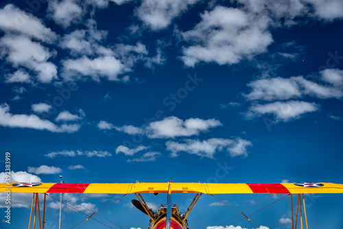 the top wing of a red and yellow biplane against a vast blue sky with clouds, symmetrical 