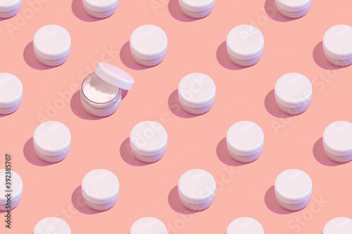 Regular pattern of closed jars of cream on a pastel pink background. Minimal skin care concept.