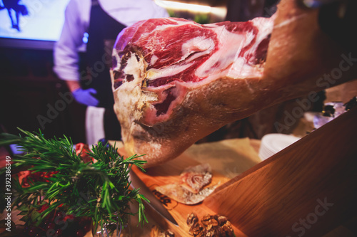 A process of slicing Hamon Jamon, traditional spanish ham on a wooden stand, slices of Parma Ham, as a part of catering on corporate party event or wedding celebration
