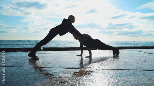 Young couple in sportswear are engaged in morning exercises against the background of the sea. The guy and the girl go in for sports together.