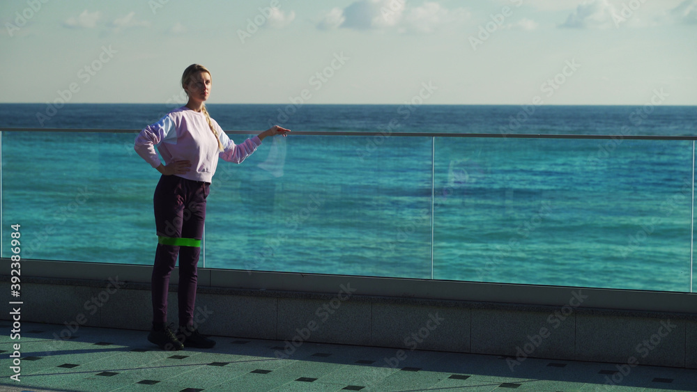 A young girl does morning exercises on a sunny day. Young blonde goes in for sports outdoors on the background of the sea. A young girl does morning exercises on a sunny day. Young blonde goes in for sports outdoors on the background of the sea.
