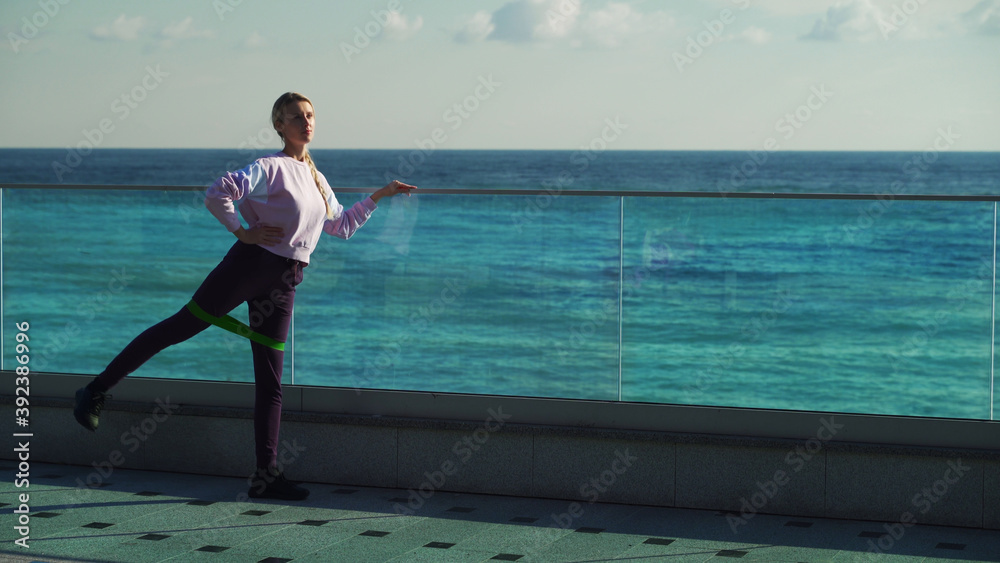 A young girl does morning exercises on a sunny day. Young blonde goes in for sports outdoors on the background of the sea.