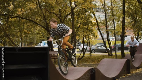 Three boys on the bike and scooters riding on the pump track in the park at sunny day. Childrens sport and healthy lifestyle concept