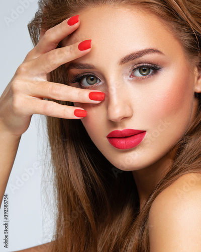 Face of young woman with red nails  lipstick and long brown hair.   Model with fashion makeup.