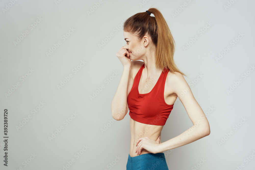 A woman in a red T-shirt on a light background is engaged in fitness gestures with her hands a slim figure A woman in a red T-shirt on a light background is engaged in fitness gestures with her hands a slim figure