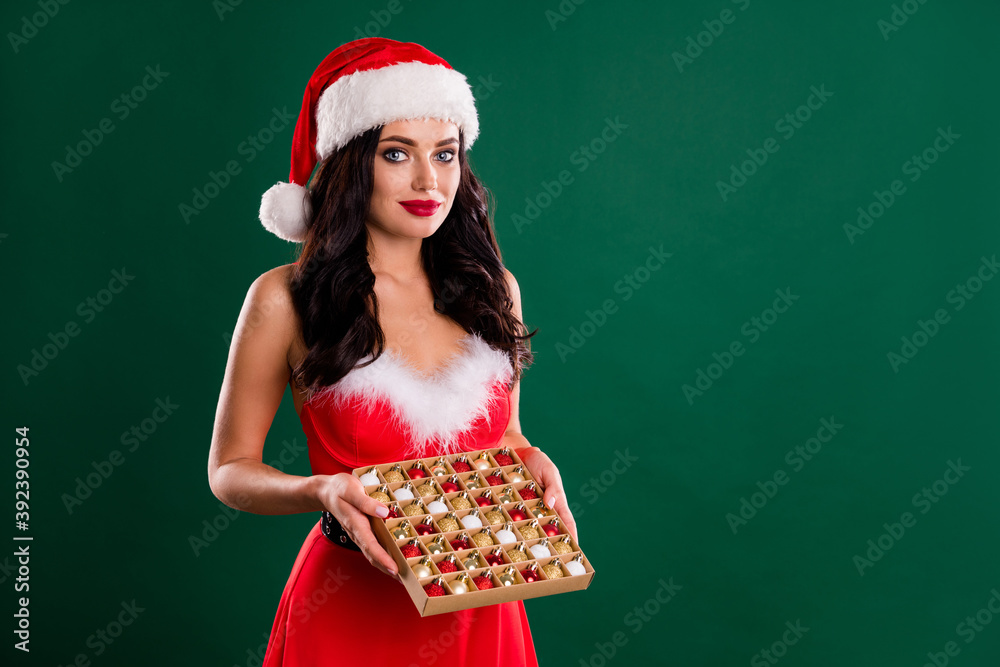 Portrait of snow girl hands hold box of tree toy red santa headwear isolated on green color background Portrait of snow girl hands hold box of tree toy red santa headwear isolated on green color background