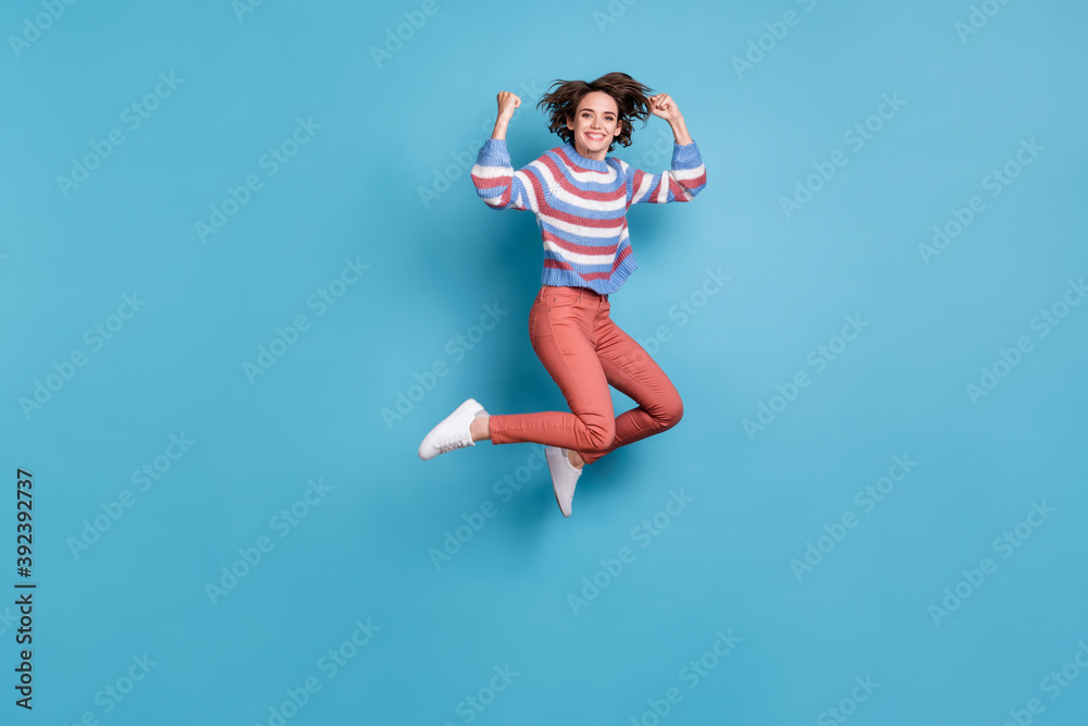 Full length body size photo of jumping up happy cheerful girl showing power smiling isolated on vibrant blue color background Full length body size photo of jumping up happy cheerful girl showing power smiling isolated on vibrant blue color background