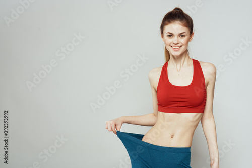A woman in a red T-shirt on a light background is engaged in fitness gestures with her hands a slim figure  © SHOTPRIME STUDIO