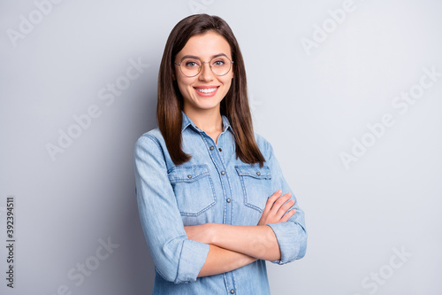 Portrait of optimistic intellectual long hairdo office worker crossed arms wear spectacles blue cloth isolated on grey background