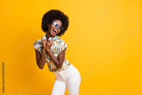 Photo of pretty cool curly hair lady dance wear headphones spectacles t-shirt trousers isolated over yellow color background