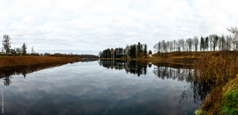 Opposite bank of lake in the autumn, cloudy sky, late autumn, bare tree silhouettes and reflections in the water