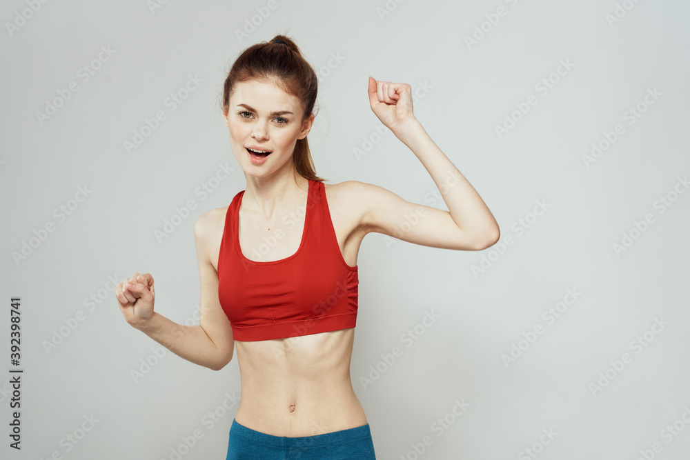 A woman in a red T-shirt on a light background is engaged in fitness gestures with her hands a slim figure 