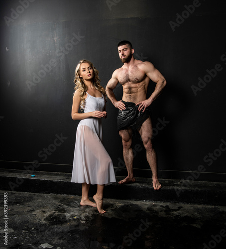 handsome athletic build man and fragile beautiful girl in white clothes on a black background