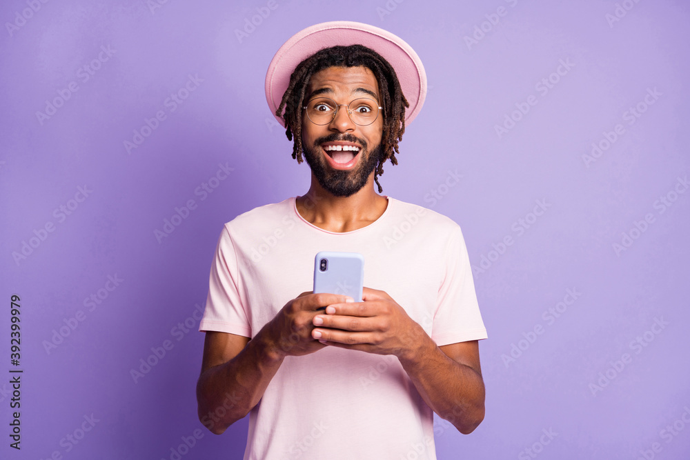 Photo portrait of excited man in pink headwear holding phone in two hands isolated on vivid violet colored background Photo portrait of excited man in pink headwear holding phone in two hands isolated on vivid violet colored background