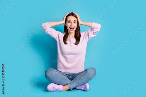 Full body size photo of cute lovely student girl sitting floor crossed legs hands head open mouth excited look luck wear violet pullover sneakers denim isolated blue color background © deagreez