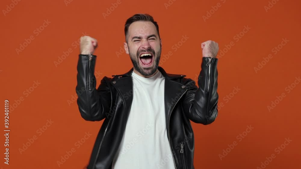 Happy joyful young bearded man 20s in casual black leather jacket isolated on orange color background studio. People lifestyle concept. Count countdown 1 2 3 one two three scream doing winner gesture Happy joyful young bearded man 20s in casual black leather jacket isolated on orange color background studio. People lifestyle concept. Count countdown 1 2 3 one two three scream doing winner gesture