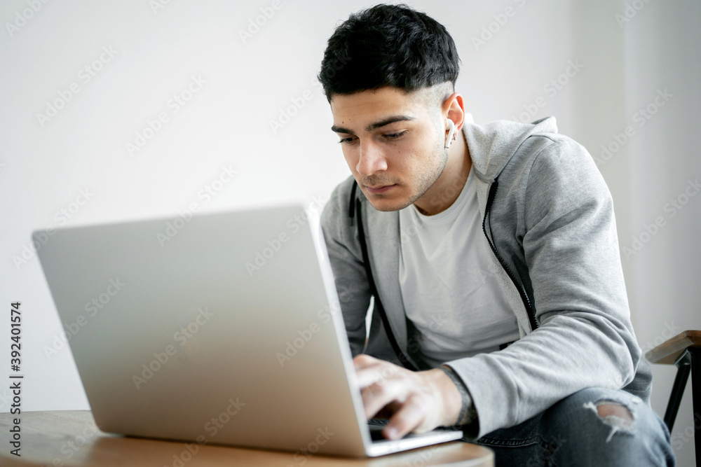 a programmer is working on a new company website at home on a laptop computer, doing an Economics assignment on his new project. comfortable clothes and has wireless headphones in his ears a programmer is working on a new company website at home on a laptop computer, doing an Economics assignment on his new project. comfortable clothes and has wireless headphones in his ears