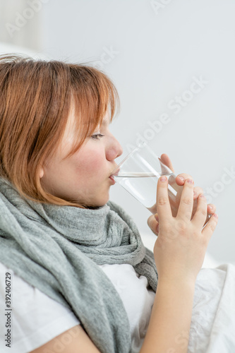Obraz na płótnie diseased girl sitting on a bed and drinking water from a glass at home