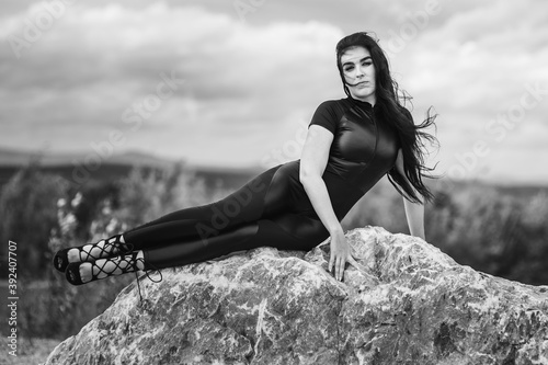 Elegant woman in black overalls is lying on big stone
