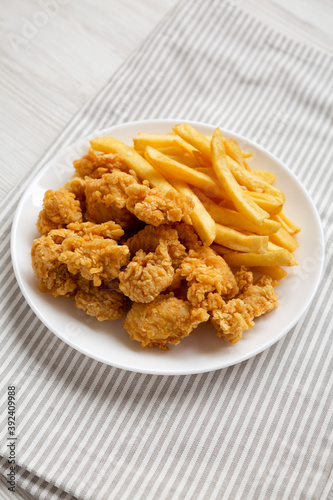 Homemade Fried Chicken Bites and French Fries on a plate, side view.