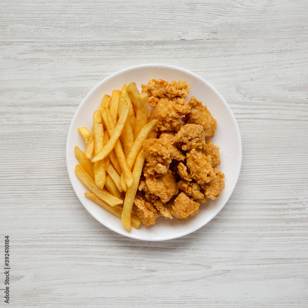 Homemade Fried Chicken Bites and French Fries on a plate on a white wooden background, overhead view. Flat lay, top view, from above. Homemade Fried Chicken Bites and French Fries on a plate on a white wooden background, overhead view. Flat lay, top view, from above.