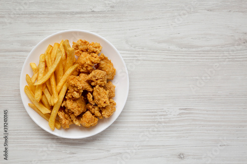 Homemade Fried Chicken Bites and French Fries on a plate on a white wooden table, overhead view. Flat lay, top view, from above. Copy space.
