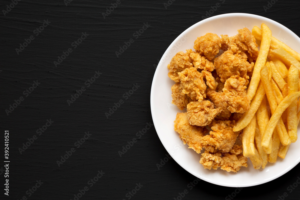 Homemade Fried Chicken Bites and French Fries on a plate on a black surface, overhead view. Flat lay, top view, from above. Copy space. Homemade Fried Chicken Bites and French Fries on a plate on a black surface, overhead view. Flat lay, top view, from above. Copy space.