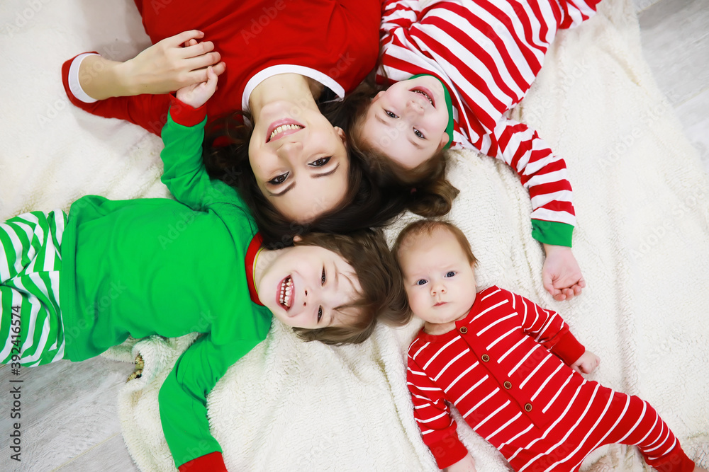 A family in striped pajamas is resting at home. Little children dressed as elves are lying on the sofa. Happy family.