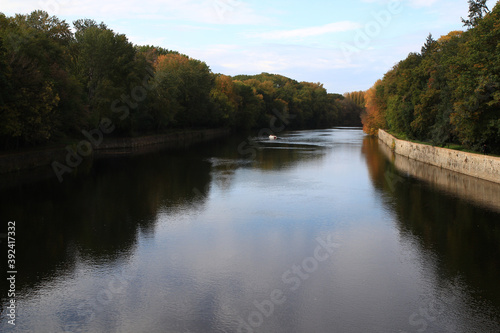 In autumn, a small boat sails peacefully on the Cher river lined with tall trees (Loire - France)