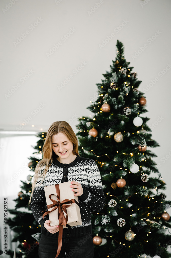 Christmas fashion photo of beautiful girl with blond hair in cozy clothes posing near Christmas tree with presents box. Happy New year concept. Christmas fashion photo of beautiful girl with blond hair in cozy clothes posing near Christmas tree with presents box. Happy New year concept.
