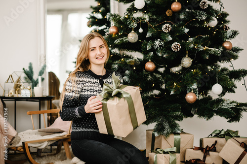 The girl opening a gift. Merry Christmas and Happy Holidays. Portrait of young woman with presents box near Christmas tree. Happy New year 2021 concept. photo