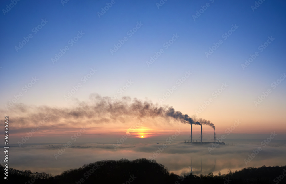 Stunning view of colorful blue and pink sky with bright rising sun at thermoelectric power plant. Thermal chimneys producing dense smoke with toxic gases into atmosphere. Concept of energy generation.