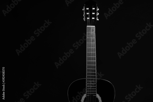 Acoustic black guitar resting against a black background with copy space